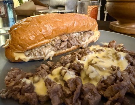 A homemade Pat's-style cheesesteak on a soft roll, next to a pile of chopped ribeye under melted homemade Whiz.